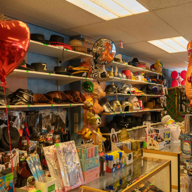 Intérieur du magasin de déguisements Abracadabra à Liège, présentant une variété de chapeaux, ballons en forme de cœur et dinosaures, masques et accessoires pour déguisements.