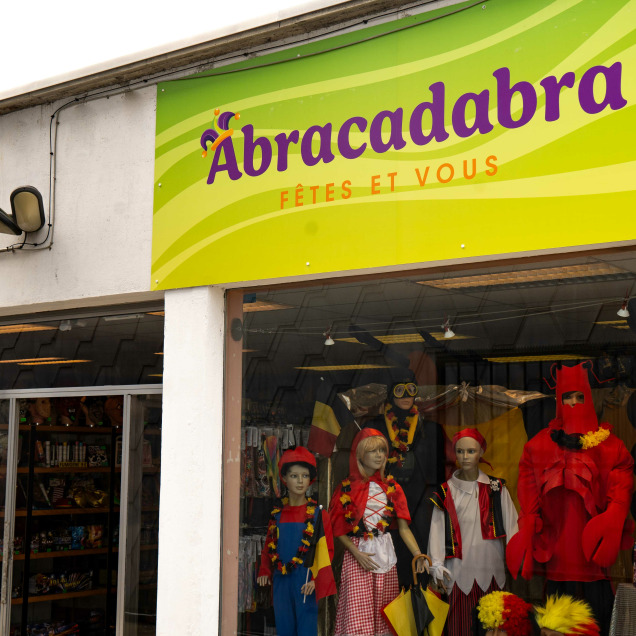 Devanture du magasin de déguisements Abracadabra à Liège avec des mannequins déguisés en vitrine et un panneau de stationnement pour la clientèle.