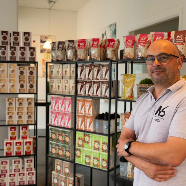 Le gérant du magasin d'alimentation sportive Nutrishop à Rocourt posant devant les étagères de compléments alimentaires et produits nutritionnels.