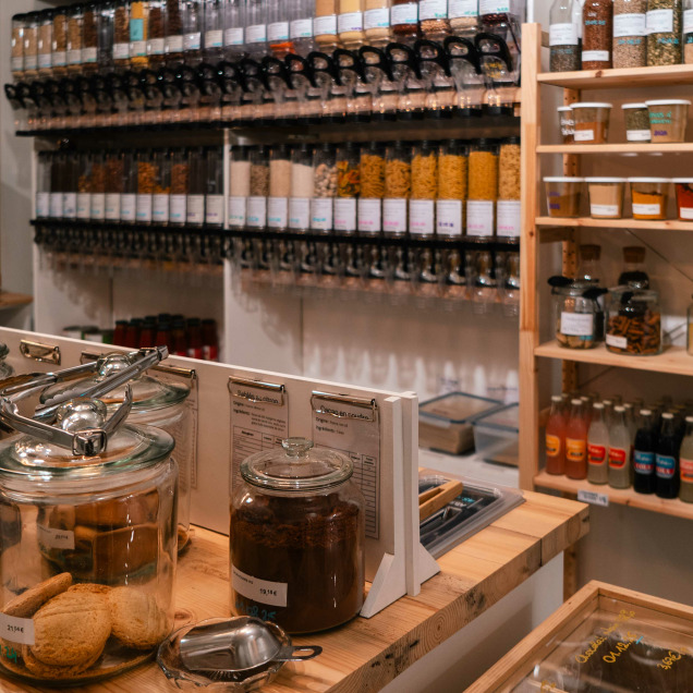 Vue intérieure de l'épicerie Tipi à Theux, avec des bocaux de biscuits en vrac et des distributeurs de produits secs sur les étagères.