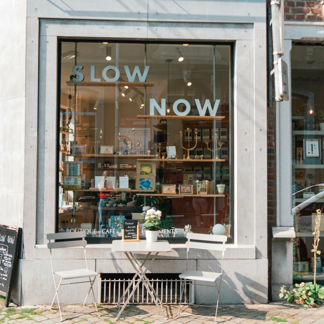 Devanture de l'épicerie Slow Now à Liège, avec une vitrine accueillante et une table extérieure pour les clients.