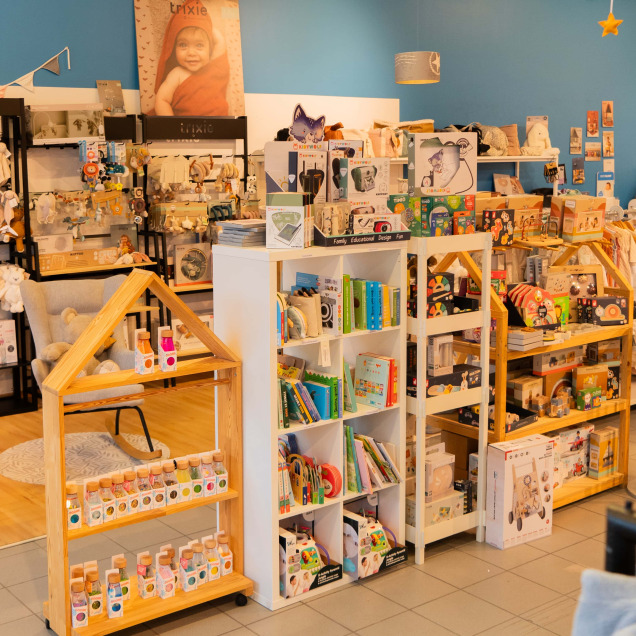 Intérieur du magasin pour bébés Ptilou à Rocourt, Belgique, montrant des jouets, vêtements et articles de puériculture bien disposés sur des étagères, créant un espace chaleureux et accueillant.