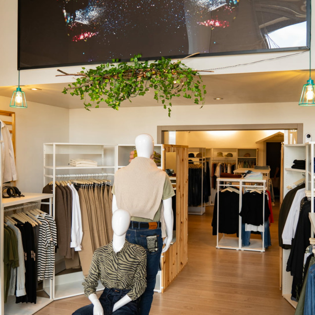 Intérieur du magasin  de vêtements Aries Clothing à Nandrin, avec une présentation de vêtements modernes, des mannequins et des étagères bien organisées