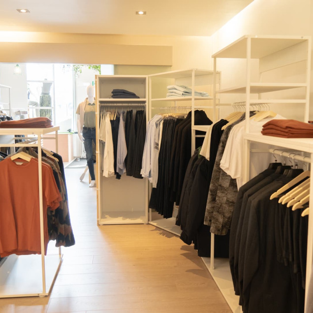 Intérieur du magasin de vêtements Aries Clothing à Nandrin avec des étagères bien organisées présentant des vêtements pour hommes et femmes.