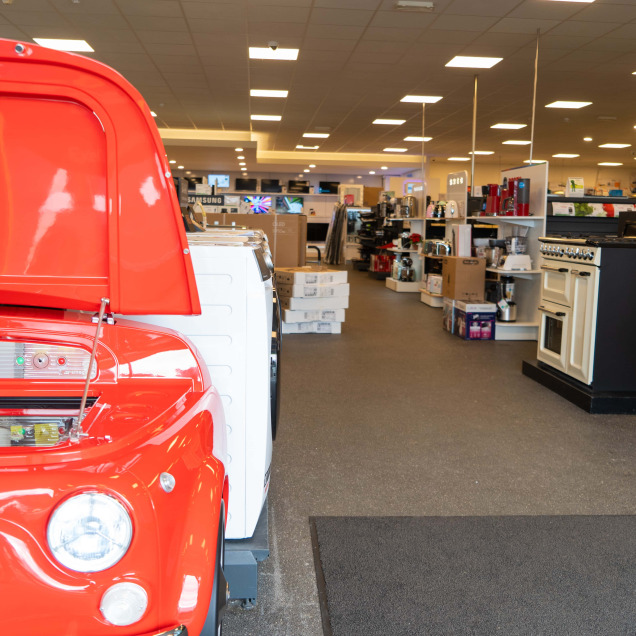 Magasin Electro TV Center à Boncelles, montrant une machine de cuisine et une voiture rouge, entourées de divers appareils électroménagers.