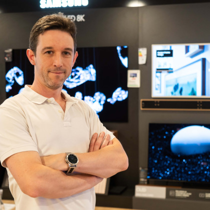 Portrait du gérant du magasin Electro TV Center à Boncelles, dans le rayon télévision, devant un écran Samsung.