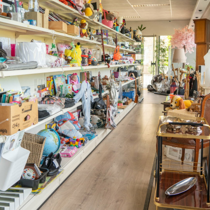 Rayons de produits de seconde main dans le magasin Boutique & Brocante à Ouffet, remplis d'objets divers tels que des jouets, vêtements et articles de décoration.