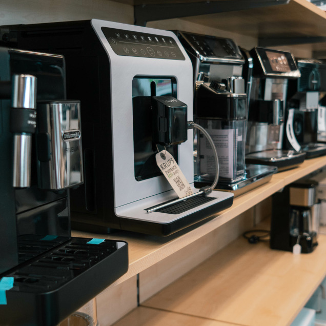 Machines à café dans le magasin d'électroménagers Maison Praillet à Visé, incluant des modèles de Delonghi, Krups et d'autres marques.