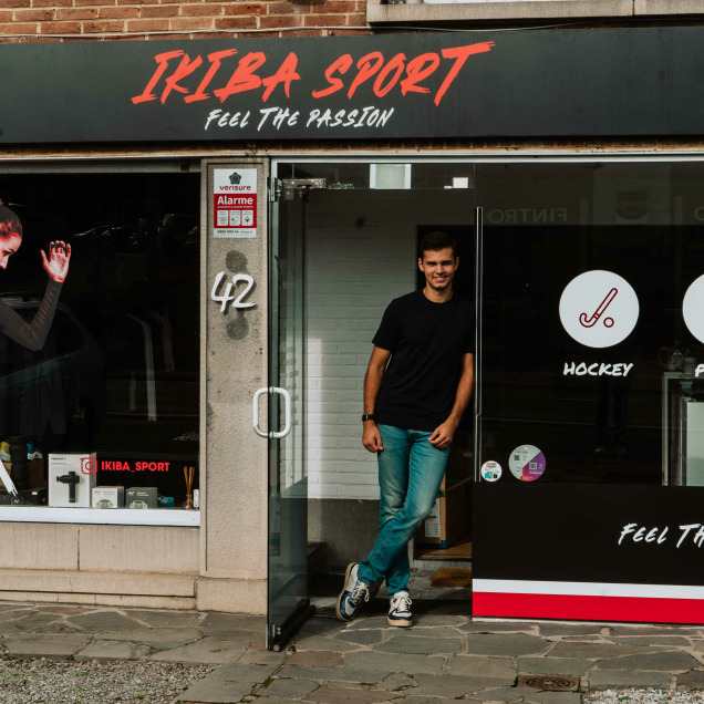 Façade du magasin Ikiba Sport à Embourg, spécialisé en hockey, running et padel, avec le gérant à l'entrée.