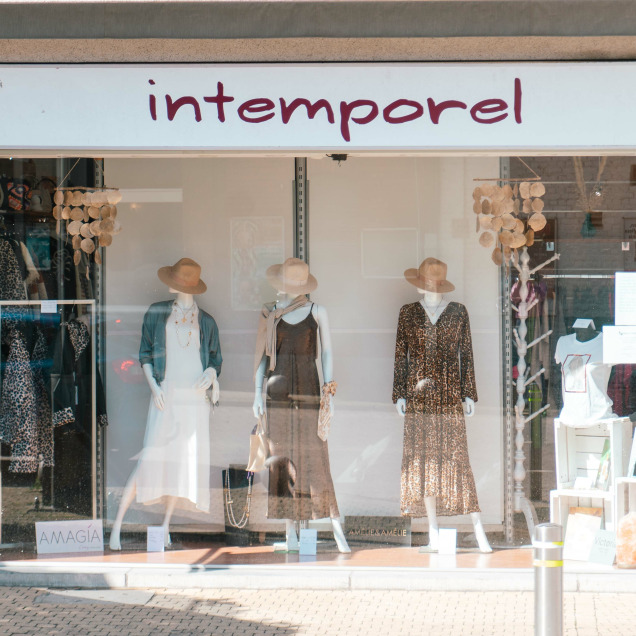 Vitrine de la boutique 'Intemporel', montrant trois mannequins habillés de robes et chapeaux d'été.