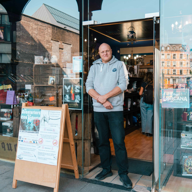 Devanture du magasin “Le Reliquaire” à Liège. Une personne se tient à l’entrée, la vitrine expose divers articles, notamment des peluches et des objets de collection.