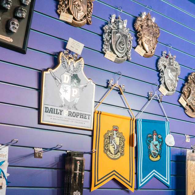 Un mur intérieur du magasin “Le Reliquaire” à Liège, décoré avec divers articles, des plaques décoratives, des masques et des bannières avec des emblèmes rappelant ceux de la série Harry Potter.