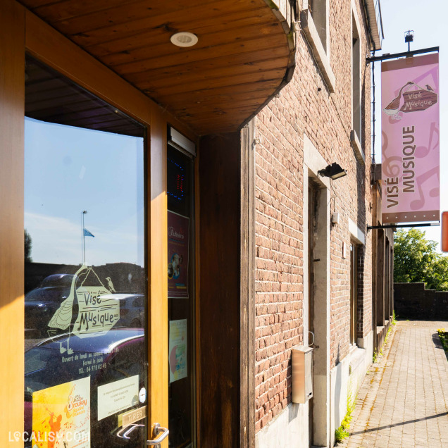 Devanture du magasin “Visé Musique” à Visé, avec une façade en bois, une porte en verre et des affiches dans la vitrine.