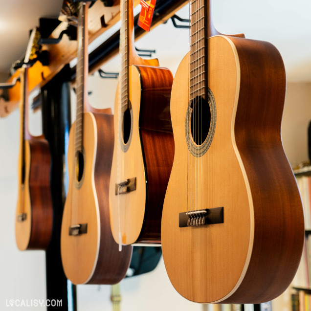 Plusieurs guitares acoustiques accrochées à un mur dans le magasin “Visé musique” à Visé . Une guitare marron clair est au premier plan, tandis que d’autres guitares se trouvent en arrière-plan, créant une impression de profondeur.