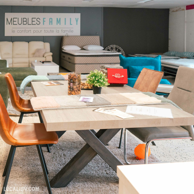 Salle d'exposition chez Meubles Family à Hannut, présentant une table à manger moderne entourée de chaises et des lits en arrière-plan.