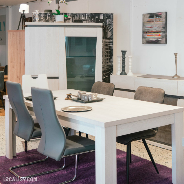 Salle à manger chez Meubles Family à Hannut, avec une table en bois clair, des chaises modernes grises, un meuble de rangement assorti et des décorations sur le thème de la maison.