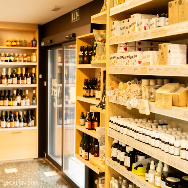 Intérieur du magasin “Au Vert G” à Boncelles. On y voit des étagères en bois bien organisées, remplies de divers produits comme des bouteilles et des boîtes.