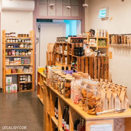 L'intérieur de “L’Épicerie d’Augustin” à Liège. On y voit des étagères en bois remplies de divers produits, des bocaux en verre contenant des aliments, et une sélection de produits exposés sur des tables.