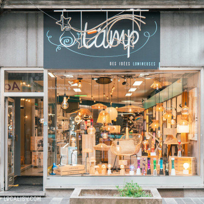 Devanture du magasin “Lamp SPRL” à Liège. La façade moderne présente une grande vitrine qui permet de voir à l’intérieur, où divers styles de lampes et luminaires sont exposés à différentes hauteurs.