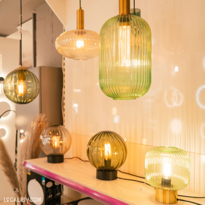 Divers styles de lampes allumées avec des designs et des couleurs variés, exposées à l’intérieur du magasin “Lamp SPRL” à Liège.