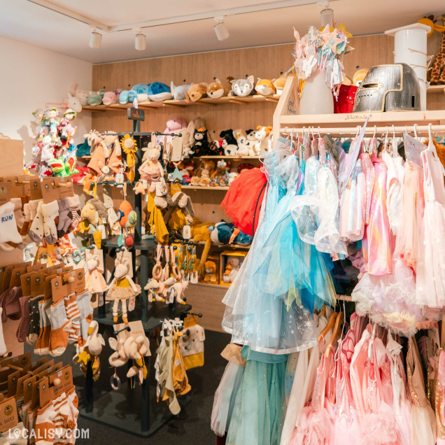 L’intérieur du magasin “Les Z’arsouilles” à Theux bien éclairé et rempli de divers articles pour enfants, notamment des peluches, des costumes et des accessoires. Les étagères et les portants sont soigneusement organisés, créant une ambiance chaleureuse et accueillante.