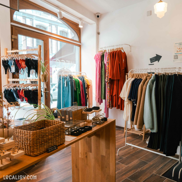 L’intérieur du magasin “WeCo Store” à Liège, avec divers articles de vêtements exposés sur des cintres et des étagères.