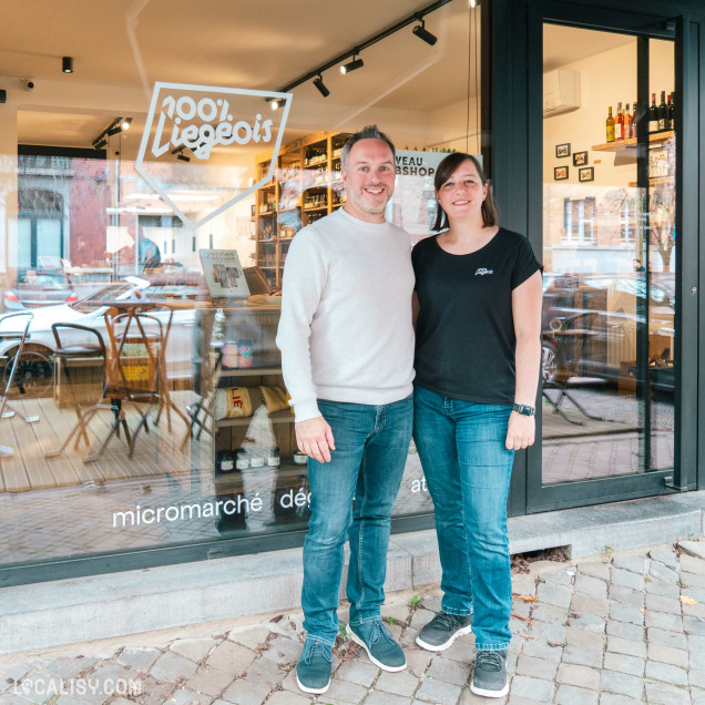 Devanture du magasin “100% Liégeois” à Liège. La vitrine expose divers articles et le logo du magasin, qui inclut un symbole de cœur, est visible au-dessus. Deux personnes se tiennent devant l’entrée.