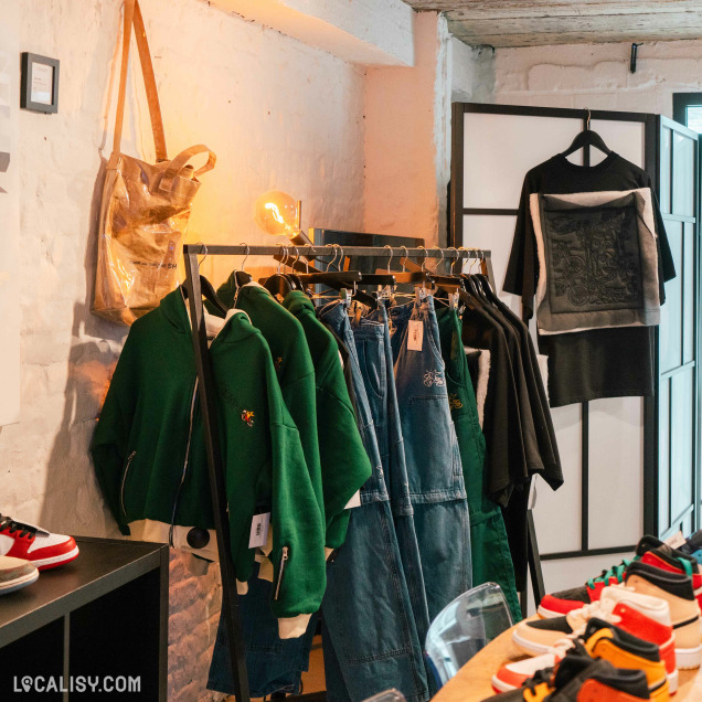 Vêtements et des chaussures exposés dans le magasin “Tenory” à Liège, avec des murs en briques apparentes et un éclairage chaleureux.