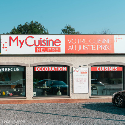 Devanture de “MyCuisine” à Neupré. L’enseigne affiche “MyCuisine NEUPRÉ” en rouge et blanc, avec le slogan “VOTRE CUISINE AU JUSTE PRIX!” en dessous. Les vitrines sont divisées en trois sections : “BARBECUE,” “DÉCORATION,” et “CUISINES,” chacune présentant des articles liés à ces catégories.