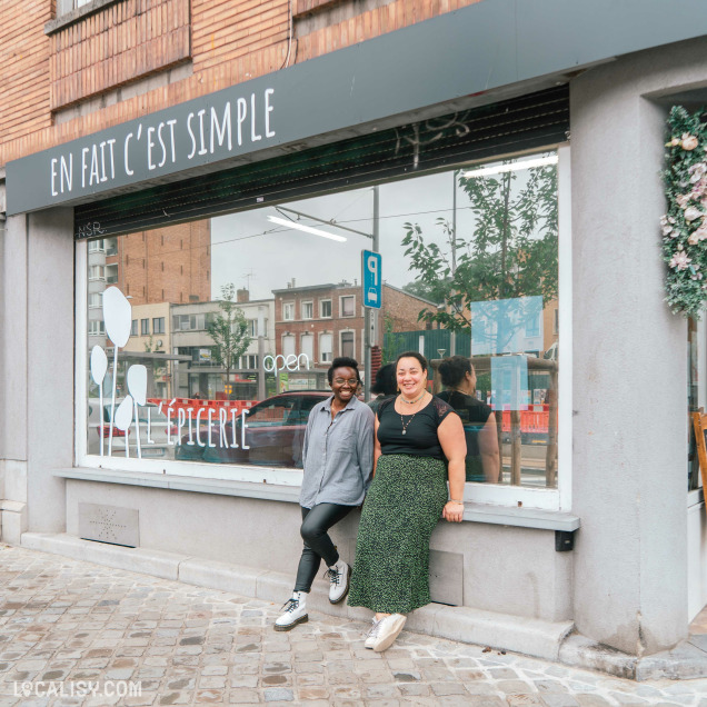 Devanture de l'épicerie “En fait C’est Simple” à Liège. La façade est dominée par une grande vitrine avec le nom de la boutique affiché en évidence sur le store. Deux personnes se tiennent devant le magasin.