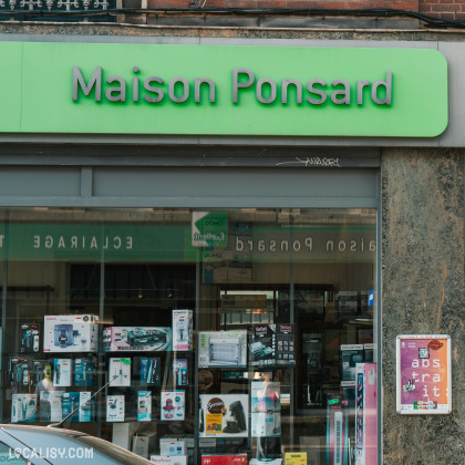 Devanture du magasin “Maison Ponsard” à Liège, spécialisé dans l’électronique. L’enseigne du magasin est bien visible en haut, avec des lettres blanches sur un fond vert. Les vitrines sont remplies de divers appareils électroniques et d’affiches promotionnelles.