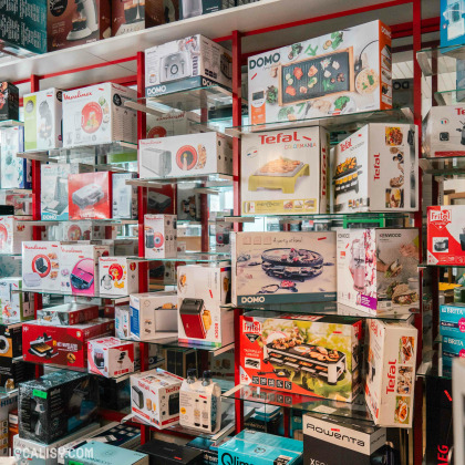 L’intérieur du magasin “Maison Ponsard” à Liège avec plusieurs étagères remplies de divers appareils de cuisine emballés, tels que des grills, des mixeurs, des machines à café et des robots culinaires. Les marques visibles incluent Tefal, Domo et Rowenta.