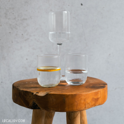 Trois verres en verre côtelé, dont deux à eau et un à vin, sont posés sur un tabouret en bois, représentant l'élégance des articles disponibles chez l'e-commerce Sista à Aywaille