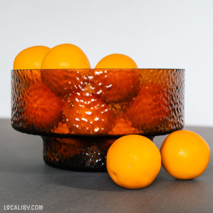 Sur cette photo, un bol texturé en verre ambré est rempli d'oranges, illustrant l'esthétique élégante et colorée des objets de décoration disponibles chez l'e-commerce Sista à Aywaille.