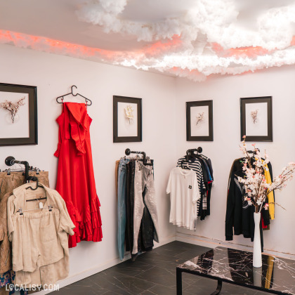 L'intérieur de Dictame, magasin de seconde main, à Liège présente un décor nuageux et des vêtements élégamment exposés, incluant une robe rouge et divers articles de mode.