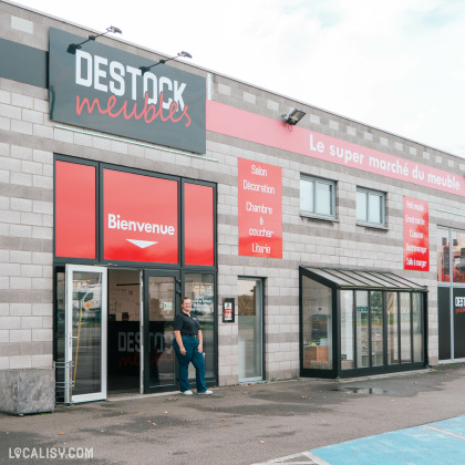 La façade du magasin Destock Meubles à Seraing affiche un grand panneau "Bienvenue", avec une employée devant l'entrée.