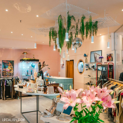 L'intérieur de Beau Bizarre, une friperie moderne à Liège, présente une décoration élégante avec des plantes suspendues, des accessoires variés et des vêtements soigneusement exposés.