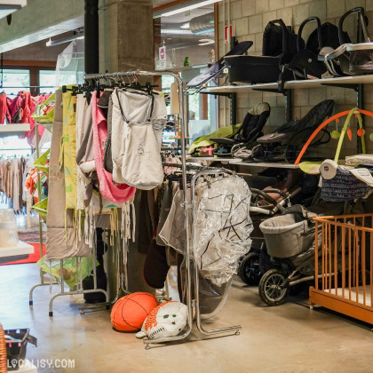 L’intérieur du magasin “Try’Fouille” à Herve avec divers articles en vente, notamment des vêtements suspendus sur des portants, des sacs, des poussettes pour bébés et des équipements sportifs au sol.