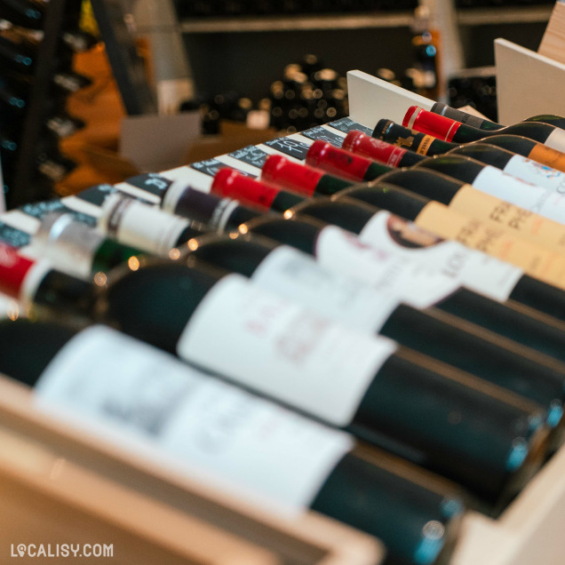 Un gros plan sur un assortiment de bouteilles de vin dans le magasin “Maag Vins” à Visé. L’accent est mis sur les étiquettes et les bouchons des bouteilles, qui sont disposées horizontalement et semblent être soigneusement organisées.