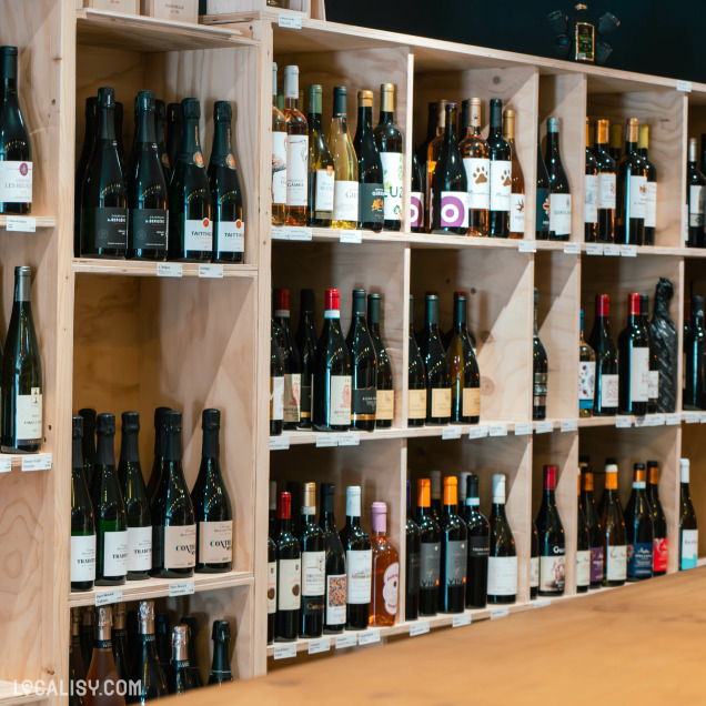 Des étagères en bois bien organisées, remplies de diverses bouteilles de vin. Chaque bouteille est placée debout, permettant une visibilité claire des étiquettes à l’intérieur du magasin “MC Vins” à Theux.