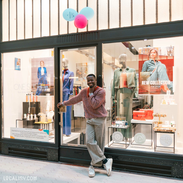 Devanture du magasin “One Such” à Liège avec des mannequins habillés avec des vêtements à la mode exposés dans la vitrine, ainsi que des produits sur des étagères. Une personne entre dans le magasin, et au-dessus de l’entrée, il y a des ballons colorés attachés aux barres.