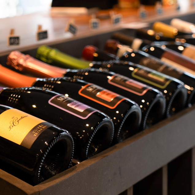 Une sélection de bouteilles de vin exposées sur une étagère du magasin “Spesa Cucina” à Theux. Les bouteilles sont disposées en ligne diagonale, créant une perspective intéressante. Chaque bouteille a une étiquette et une couleur différentes, indiquant une variété.