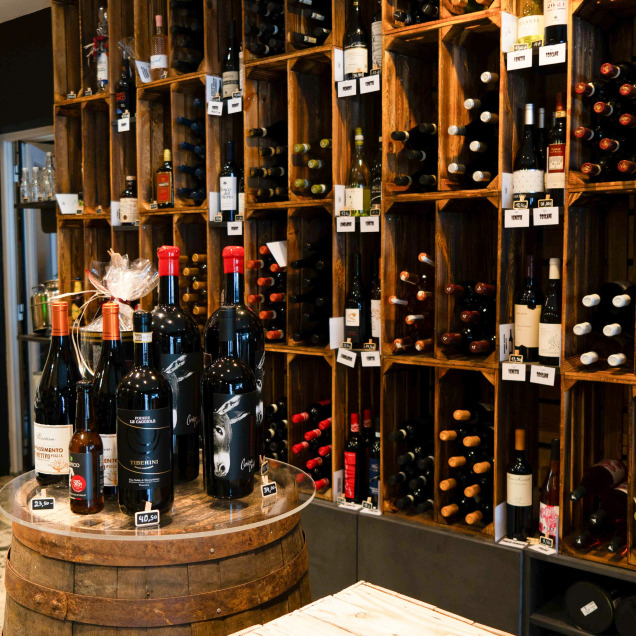 L’intérieur du magasin “Spesa Cucina” à Theux avec de nombreuses étagères en bois remplies de bouteilles de vin. Au premier plan, un tonneau en bois avec plusieurs bouteilles de vin posées dessus.