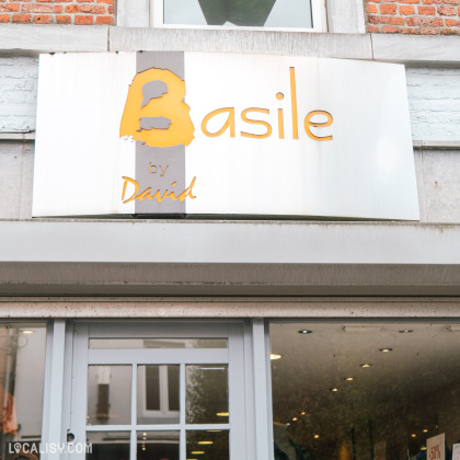 Devanture du magasin “Basile” à Ans. L’enseigne est montée sur le mur extérieur au-dessus de l’entrée du magasin. Le fond de l’enseigne est blanc, avec “Basile” écrit en grandes lettres majuscules et audacieuses.