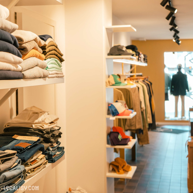 Intérieur du magasin "Monsieur Lascar" avec des étagères de casquettes et de pulls