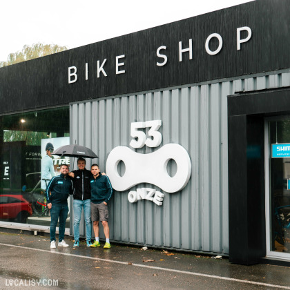 Devanture du magasin de vélos “53Onze Ans” à Ans. La façade est moderne, avec des panneaux métalliques ondulés gris foncé et de grandes fenêtres.