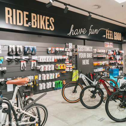 Une exposition de vélos et d’accessoires associés au magasin de vélos “53Onze Ans” à Ans. Sur le mur, on peut lire des phrases motivantes telles que “RIDE BIKES,” “have fun,” et “FEEL GOOD.”