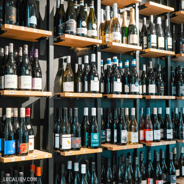 Des bouteilles, probablement de vin ou d’autres boissons, disposées sur des étagères en bois. Les étagères sont organisées en grille contre un fond sombre, mettant en valeur les bouteilles à “La Fromagerie des Vennes” à Liège