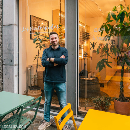 Devanture du magasin “Les Vintrépides” à Liège. À travers la grande vitrine, on aperçoit des étagères avec des articles, probablement des bouteilles de vin. Une personne se tient devant la vitrine, et deux tables colorées sont placées à l’extérieur près de l’entrée.