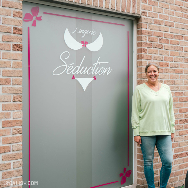 Devanture du magasin “Lingerie Séduction” à Neupré. L’enseigne est sur un fond gris avec des éléments décoratifs, y compris un motif de papillon et des accents roses.